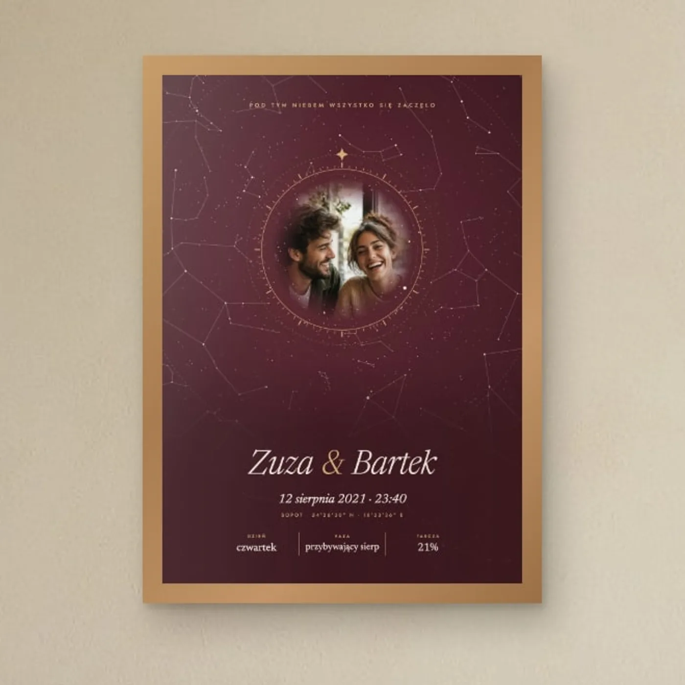Bordowy plakat z niebem nad Sopotem i zdjęciem pary w złotym pierścieniu, w drewnianej ramie nad łóżkiem